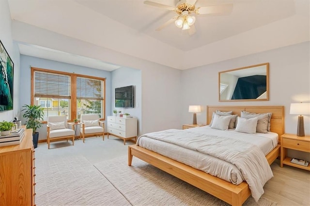 bedroom featuring a raised ceiling, light wood-type flooring, and ceiling fan