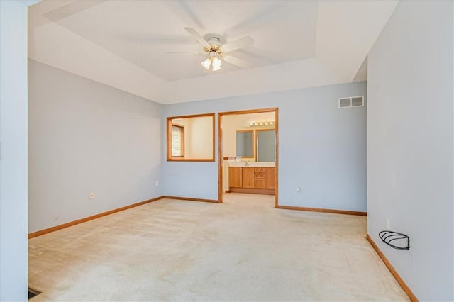 unfurnished room with ceiling fan, a tray ceiling, and light carpet