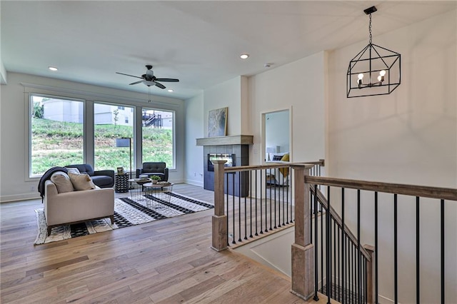 living room featuring a tile fireplace, light hardwood / wood-style floors, and ceiling fan with notable chandelier