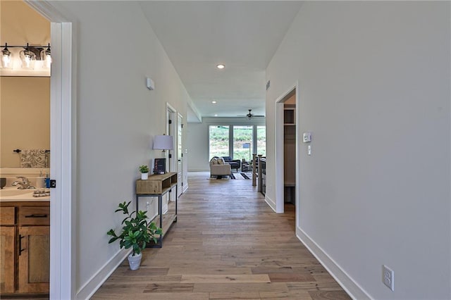corridor with light wood finished floors, recessed lighting, baseboards, and a sink