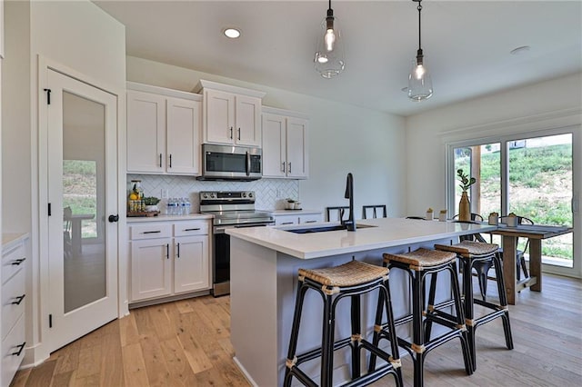 kitchen with a center island with sink, light wood-style flooring, stainless steel appliances, decorative backsplash, and white cabinetry