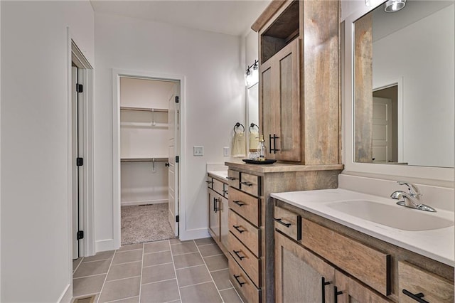 bathroom with baseboards, two vanities, a sink, a spacious closet, and tile patterned floors