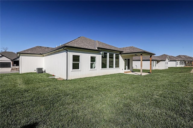 rear view of property featuring a yard, central air condition unit, roof with shingles, and a patio area