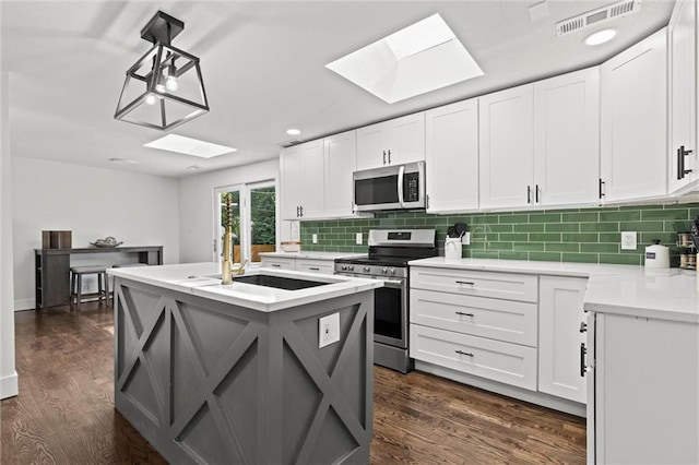 kitchen featuring appliances with stainless steel finishes, pendant lighting, tasteful backsplash, white cabinets, and a center island with sink