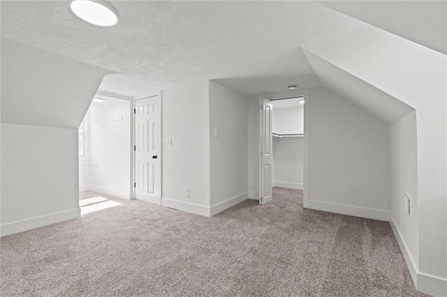 bonus room featuring lofted ceiling, light colored carpet, and a textured ceiling