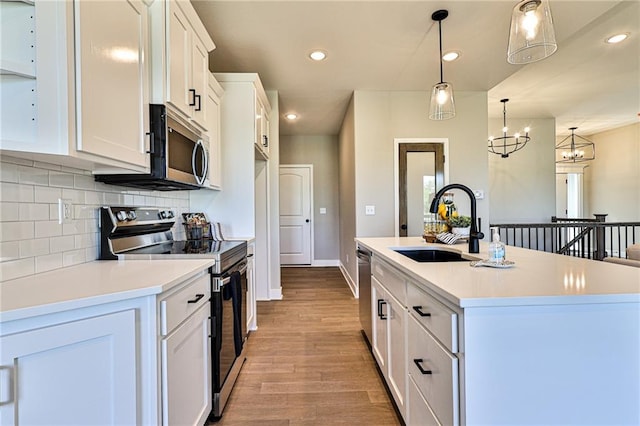 kitchen with hanging light fixtures, white cabinets, stainless steel appliances, light hardwood / wood-style flooring, and a kitchen island with sink