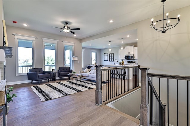 living room featuring ceiling fan with notable chandelier, wood finished floors, baseboards, and recessed lighting