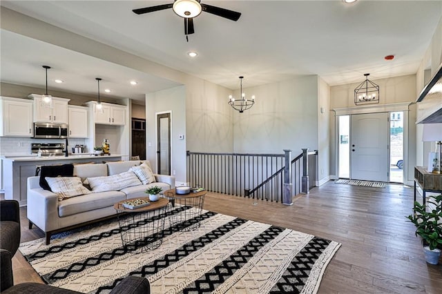 living area featuring ceiling fan with notable chandelier, wood finished floors, baseboards, and recessed lighting