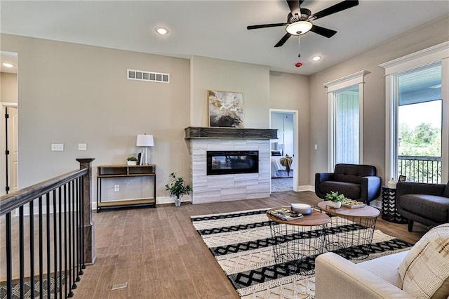 living area featuring a ceiling fan, a fireplace, wood finished floors, baseboards, and visible vents