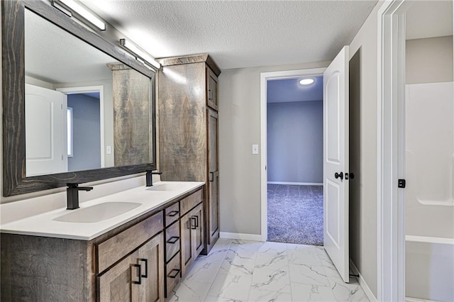 full bathroom with marble finish floor, a sink, baseboards, and a textured ceiling