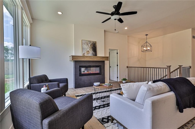 living room featuring ceiling fan with notable chandelier, a fireplace, and light hardwood / wood-style flooring