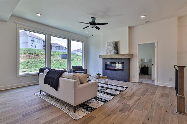 living area featuring a tiled fireplace, wood finished floors, baseboards, and ceiling fan