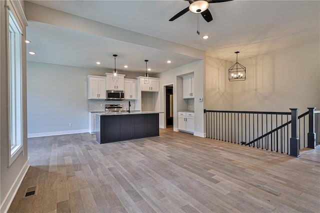 kitchen featuring pendant lighting, an island with sink, white cabinetry, stainless steel appliances, and light hardwood / wood-style floors