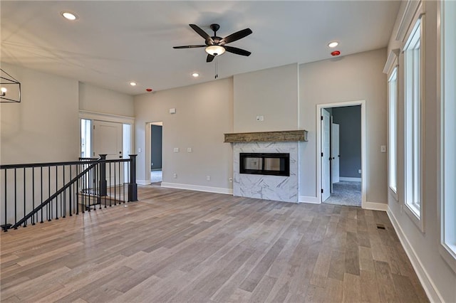 unfurnished living room with ceiling fan with notable chandelier, a high end fireplace, and hardwood / wood-style flooring