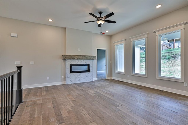 unfurnished living room featuring wood-type flooring, ceiling fan, and a premium fireplace