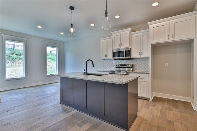 kitchen with an island with sink, decorative light fixtures, white cabinetry, stainless steel appliances, and light wood-type flooring