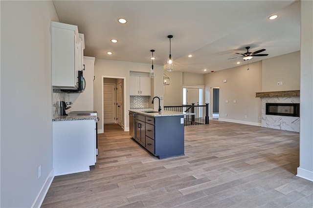 kitchen with light wood-type flooring, white cabinets, a center island with sink, white range oven, and decorative light fixtures