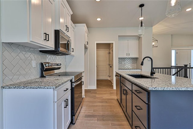 kitchen with appliances with stainless steel finishes, hanging light fixtures, white cabinetry, light stone counters, and light hardwood / wood-style flooring