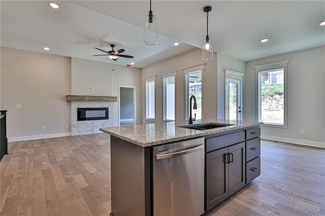 kitchen with light stone counters, dishwasher, light hardwood / wood-style flooring, a kitchen island with sink, and sink