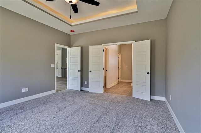 unfurnished bedroom with ceiling fan, light colored carpet, and a raised ceiling