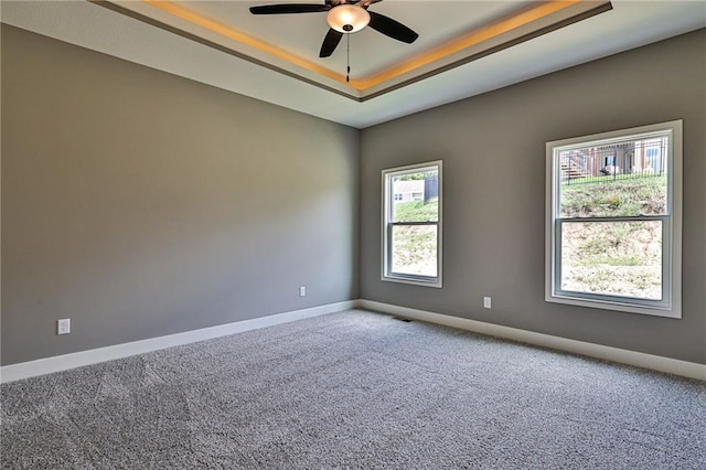 carpeted spare room with baseboards, ceiling fan, visible vents, and a raised ceiling