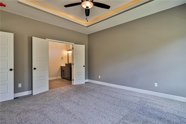 unfurnished bedroom with baseboards, a tray ceiling, and carpet