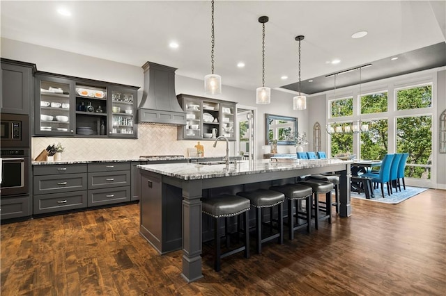 2804 NW Nutall Ct, Lees Summit, MO 64081 - kitchen featuring appliances with stainless steel finishes, custom exhaust hood, a kitchen breakfast bar, light stone countertops, and an island with sink
