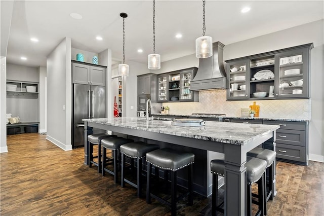 kitchen with high end fridge, a spacious island, decorative light fixtures, custom exhaust hood, and dark hardwood / wood-style floors