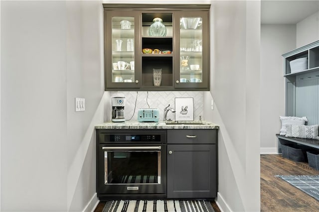 bar with light stone countertops, oven, sink, decorative backsplash, and dark hardwood / wood-style floors