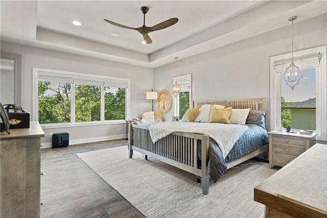 bedroom featuring hardwood / wood-style floors, ceiling fan with notable chandelier, and a raised ceiling