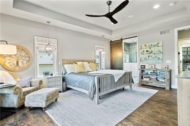 bedroom with a barn door, ceiling fan with notable chandelier, and dark hardwood / wood-style flooring