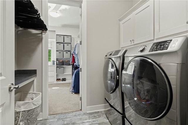 clothes washing area featuring washing machine and dryer, light hardwood / wood-style floors, and cabinets