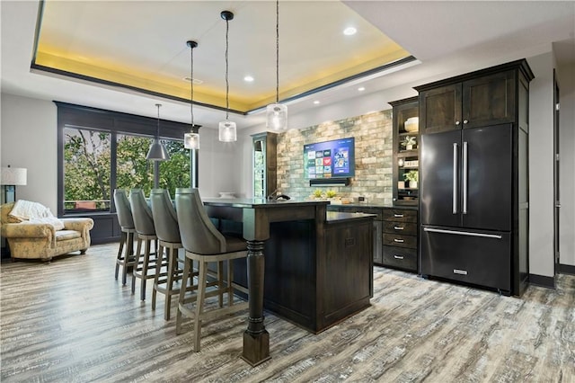 bar with light hardwood / wood-style floors, a tray ceiling, decorative light fixtures, and built in refrigerator