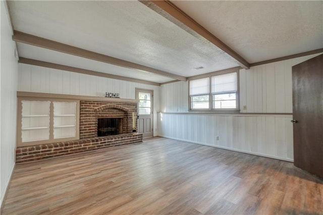 unfurnished living room featuring beam ceiling, a brick fireplace, light hardwood / wood-style flooring, and a textured ceiling