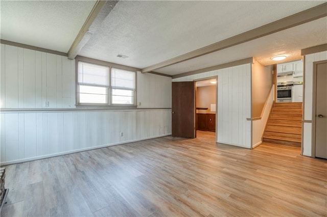 interior space with beam ceiling, a textured ceiling, and light wood-type flooring