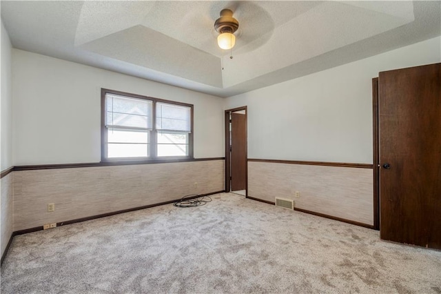 carpeted spare room featuring a raised ceiling, ceiling fan, and a textured ceiling