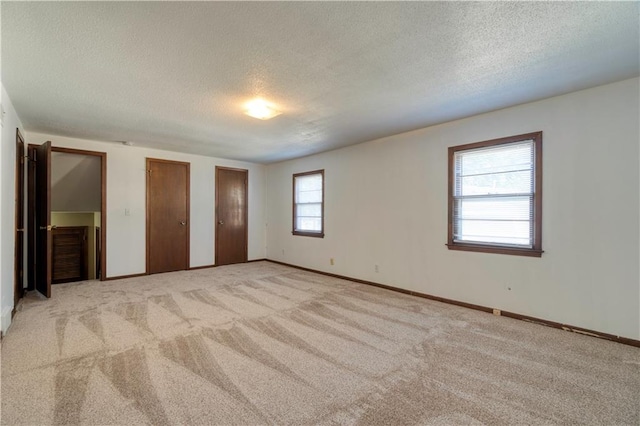 unfurnished bedroom featuring light carpet, a textured ceiling, and multiple closets