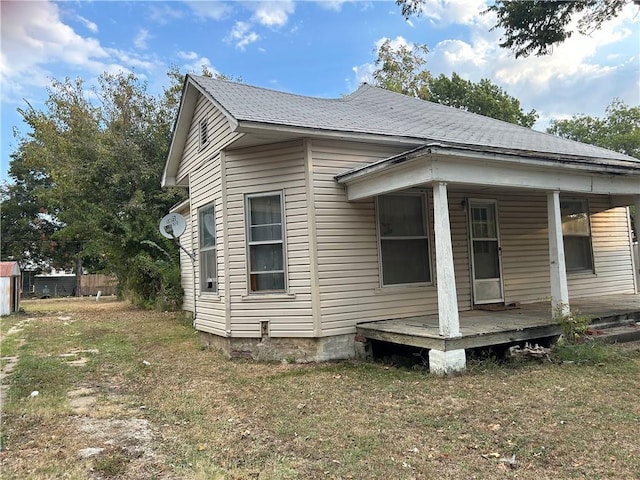 rear view of property featuring a shingled roof, a porch, and a lawn