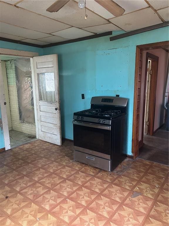 kitchen with stainless steel gas range, a paneled ceiling, ceiling fan, and baseboards