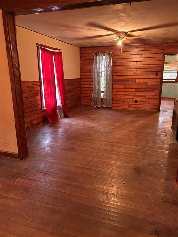 unfurnished living room featuring wood walls, wood-type flooring, a ceiling fan, and wainscoting