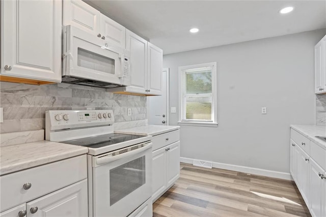 kitchen with white appliances, backsplash, white cabinetry, light stone counters, and light hardwood / wood-style flooring