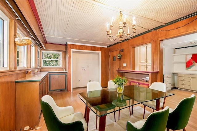 dining area with an inviting chandelier, light hardwood / wood-style flooring, and wooden walls