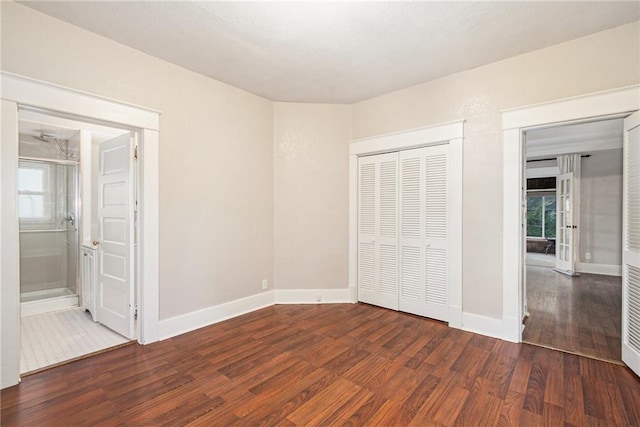 unfurnished bedroom featuring a closet, ensuite bath, and dark hardwood / wood-style floors