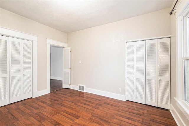 unfurnished bedroom featuring dark hardwood / wood-style flooring and two closets