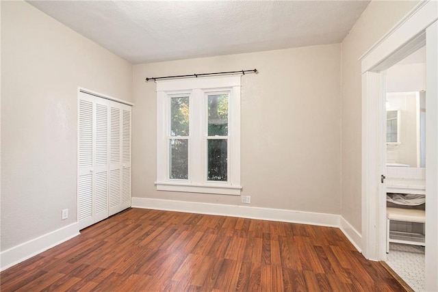 unfurnished bedroom featuring ensuite bath, dark wood-type flooring, and a closet