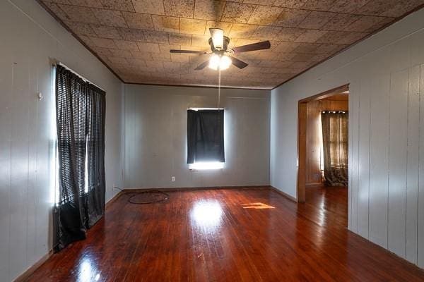 empty room featuring hardwood / wood-style flooring, wooden walls, and ceiling fan