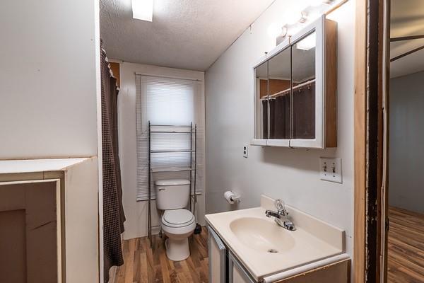 bathroom with a textured ceiling, wood-type flooring, vanity, and toilet