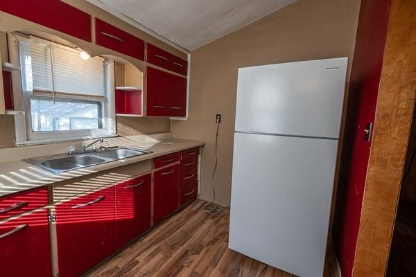 kitchen featuring white fridge, vaulted ceiling, sink, and wood-type flooring