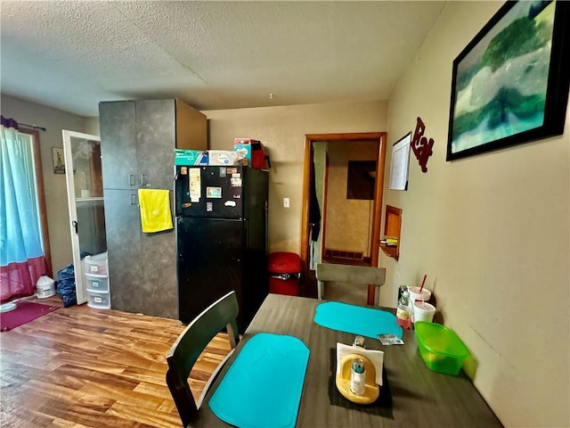 kitchen with black fridge, a textured ceiling, and light hardwood / wood-style floors