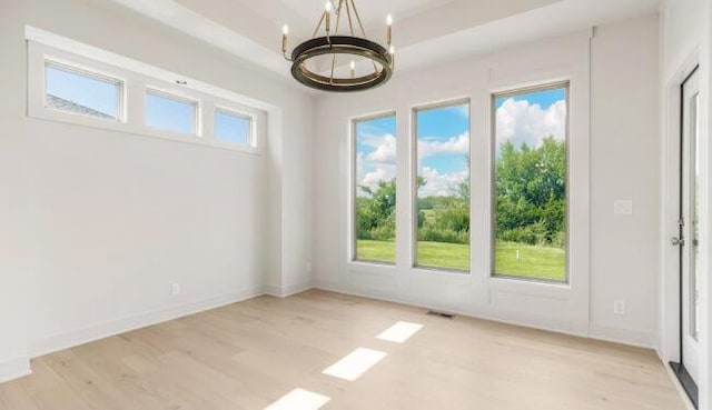 empty room featuring plenty of natural light, a chandelier, and light wood-type flooring